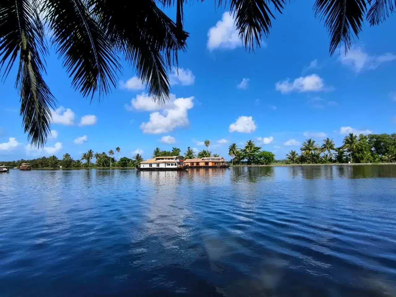 Blue Alleppey backwaters with boats beneath a tropical sky
